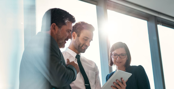3 office workers looking over an electronic device